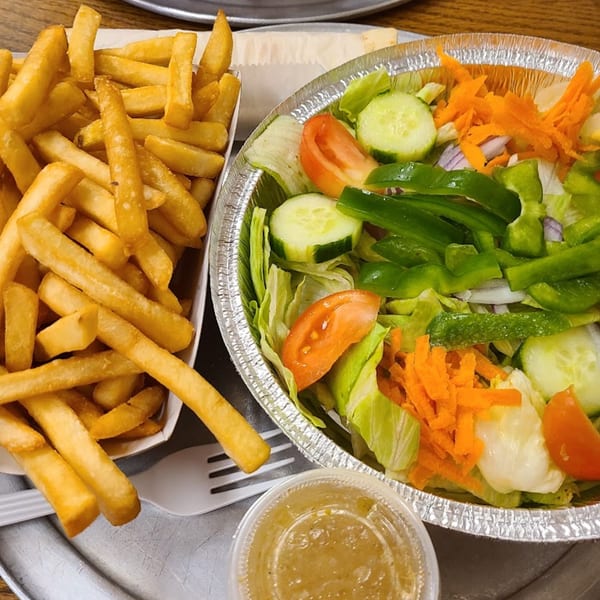 Golden french fries in a paper tray next to a fresh garden salad with dressing.