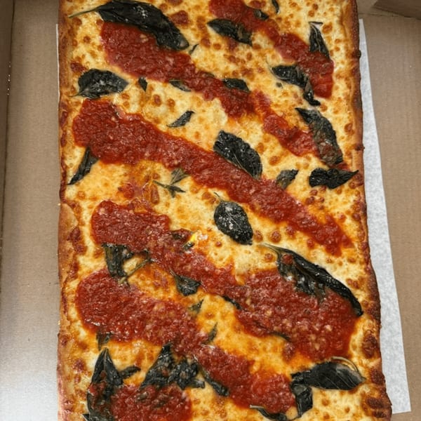 Close-up of a rectangular NYC Village Pizza with red sauce stripes, cheese, and basil.
