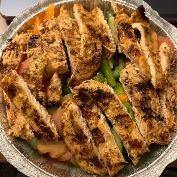 Grilled chicken strips over a fresh salad with green peppers and carrots in a foil container.