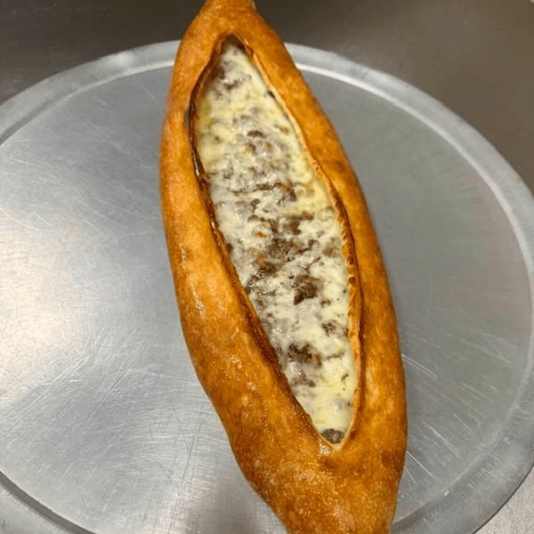 A golden-brown, boat-shaped pizza with melted cheese and ground meat filling on a metal tray.